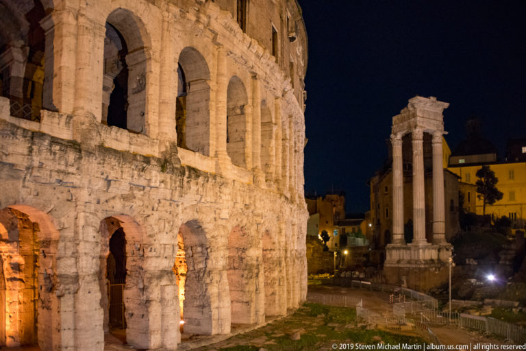Night view of the Theatre of Marcellus beside three standing columns of the Temple of Apollo Sosianus in Rome.