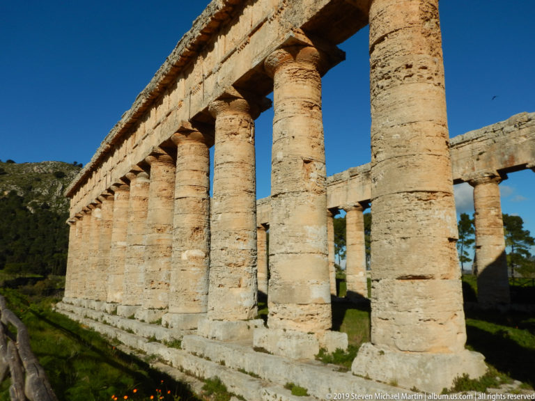Oblique view along the sunlit Doric colonnade and stepped platform of the Temple of Segesta.