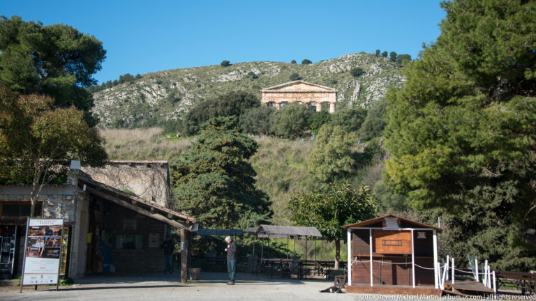 Visitor facilities at Segesta with the ancient Doric temple visible high on the wooded hillside beyond.