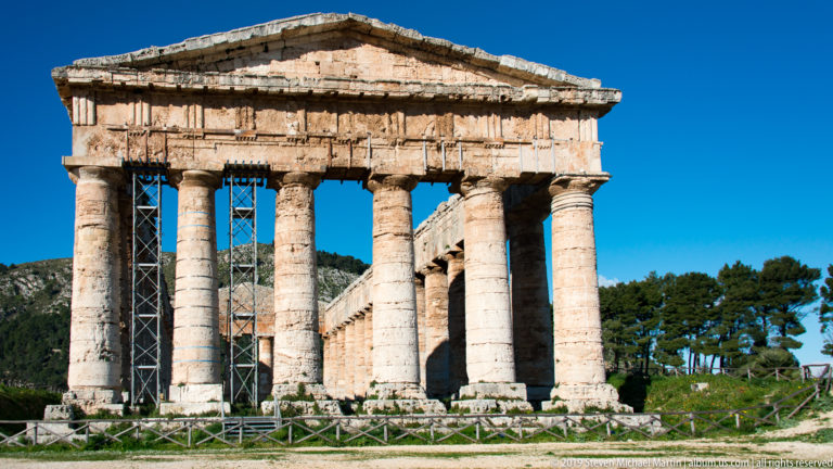 Frontal view of the Temple of Segesta with six Doric columns, pediment, and scaffolding visible behind the façade.