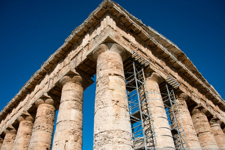 Low-angle corner of the Temple of Segesta with metal conservation scaffolding rising between Doric columns.