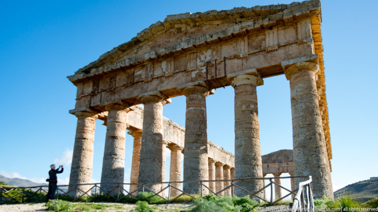 Low-angle view of massive Doric columns and entablature at the Temple of Segesta, with a visitor at left.