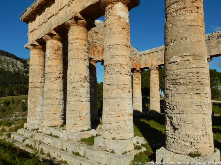 Cluster of weathered Doric columns at a corner of the Temple of Segesta with hillside visible through the open structure.
