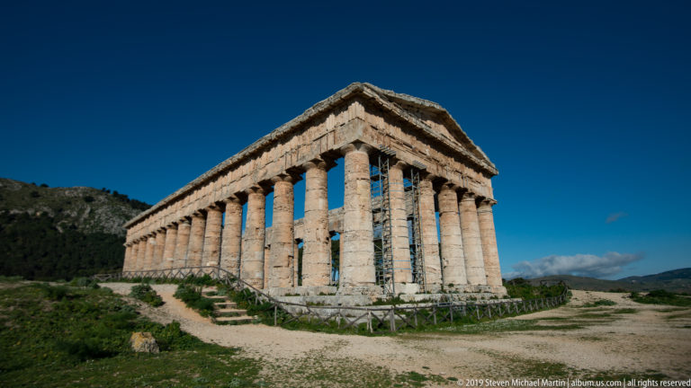 Oblique corner view of Segesta’s Doric temple with receding columns, pediment, interior scaffolding, and visitor path.