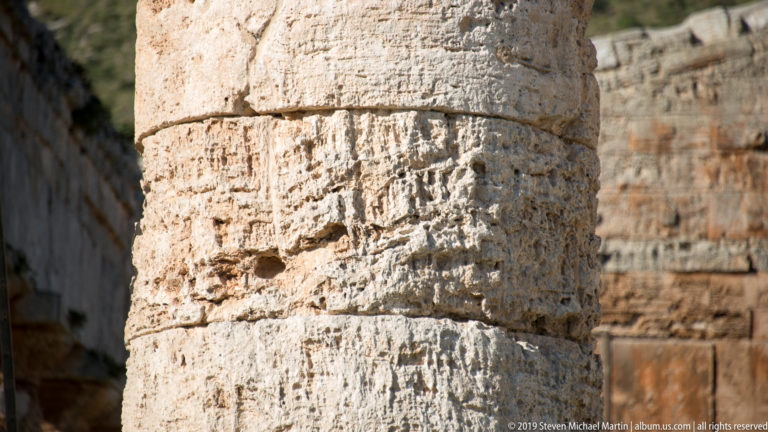 Close-up of a weathered temple column shaft showing rough stone texture, joints, and adjacent masonry.