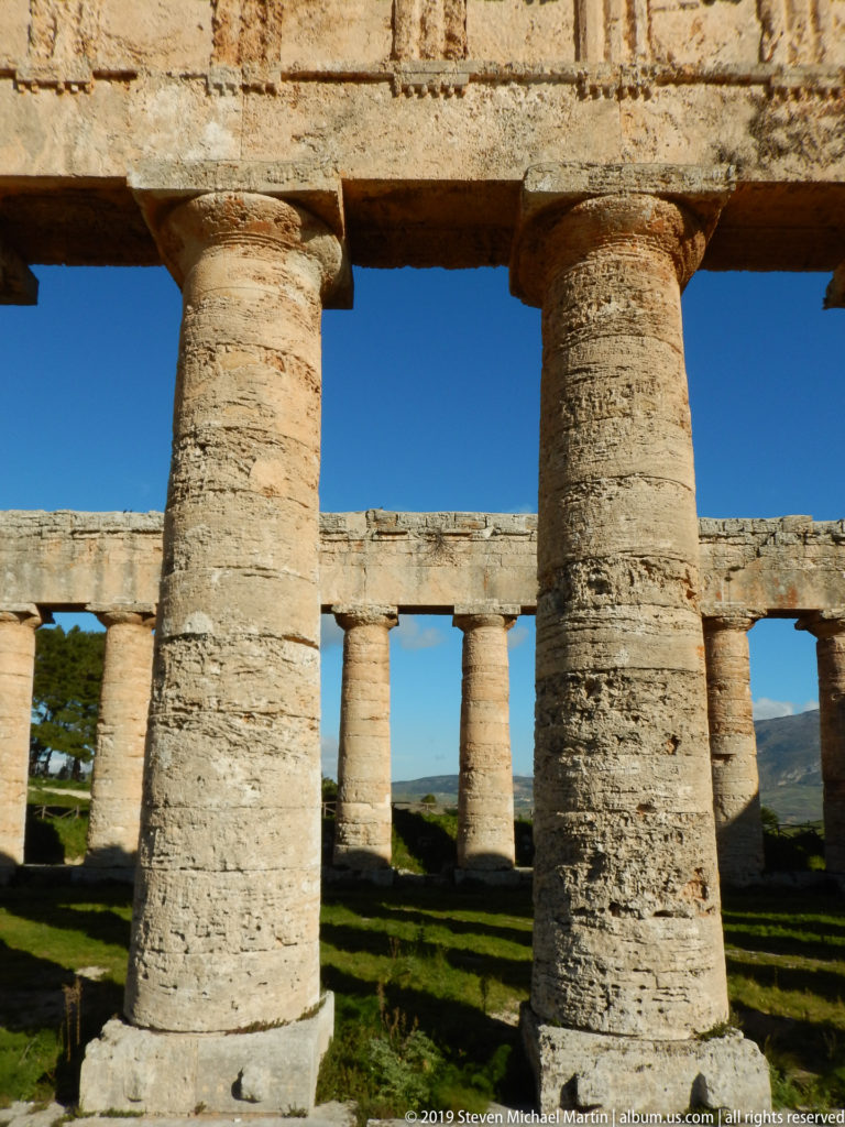Two massive Doric columns in the foreground frame the opposite colonnade and distant landscape at the Temple of Segesta.