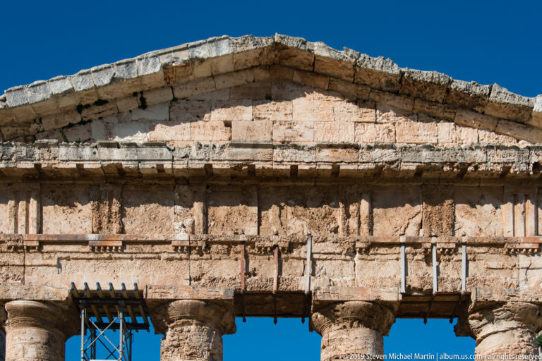 Close view of Segesta temple’s triangular pediment and weathered entablature above column capitals and supports.