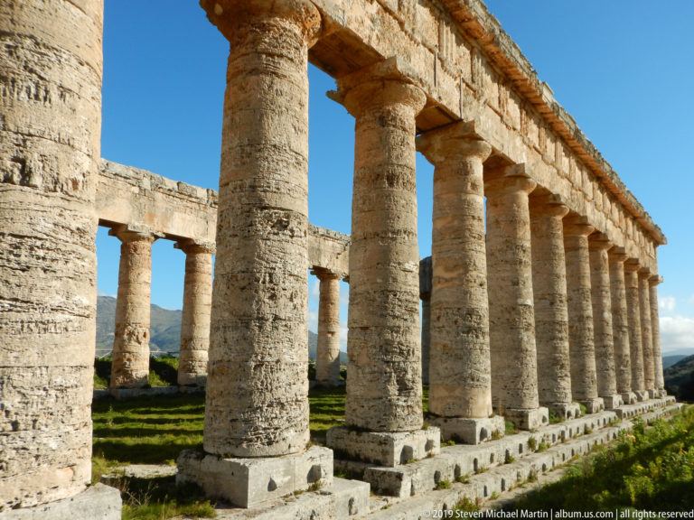 Angled view through thick Doric columns into the open interior of the Temple of Segesta, with a second colonnade beyond.