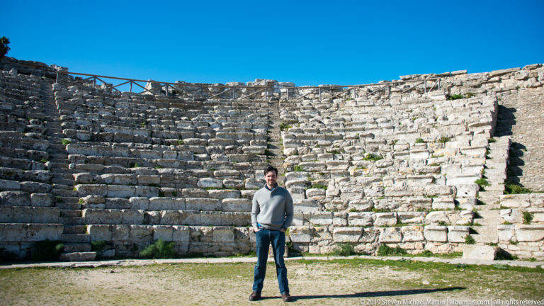 Visitor centered before the curved stone seating and retaining wall of Segesta’s ancient theater.