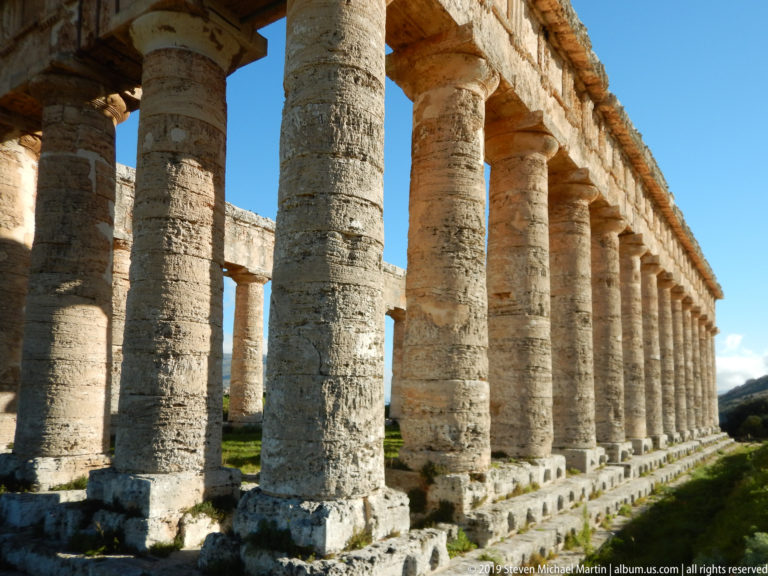 Perspective view down a receding row of weathered Doric columns beneath the entablature at the Temple of Segesta.