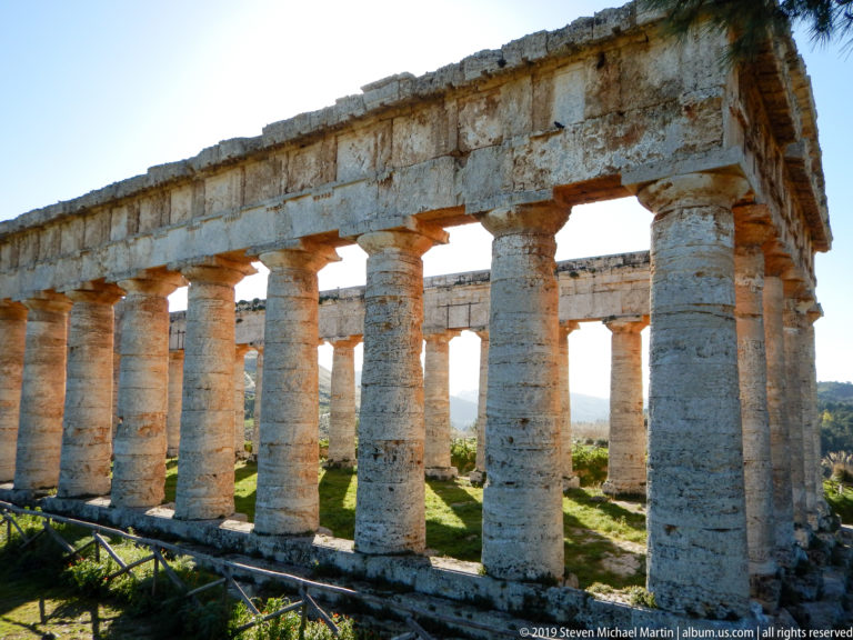 Oblique sunlit view along the Temple of Segesta’s long row of Doric columns and surviving entablature.