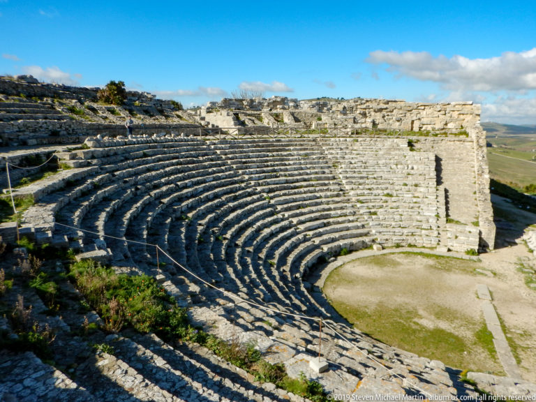 Elevated view over the curved stone seating and orchestra of the ancient theater at Segesta.