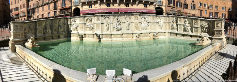 Fonte Gaia’s marble relief panels and sculpted figures surround a shallow green-water basin in Siena’s Piazza del Campo.