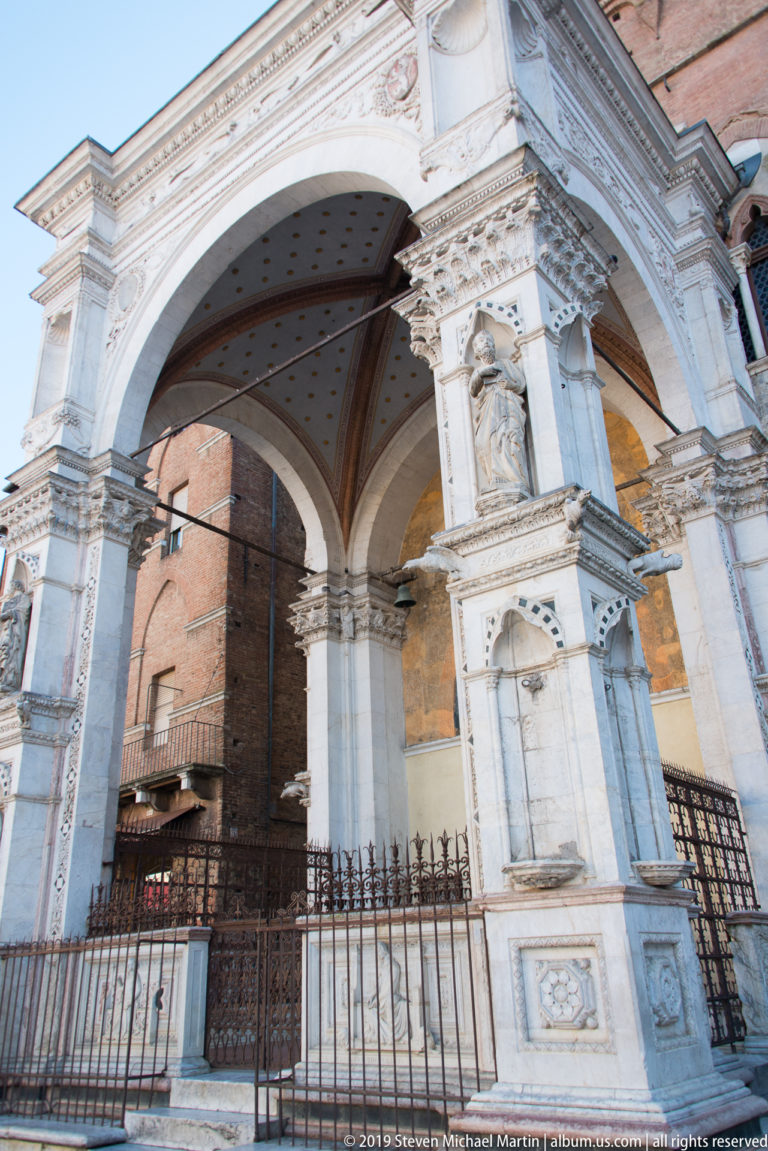 Close low-angle view of Cappella di Piazza showing marble piers, statues in niches, carved capitals, and vaulted bays.