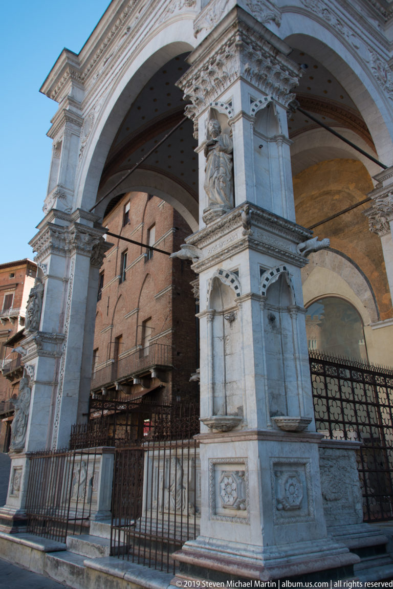 Oblique side view of Cappella di Piazza with marble arches, sculpted niches, vaulted interior, and iron railings.