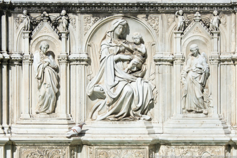 Marble relief of seated Madonna and Child in a central arch, flanked by two standing figures in narrow niches.