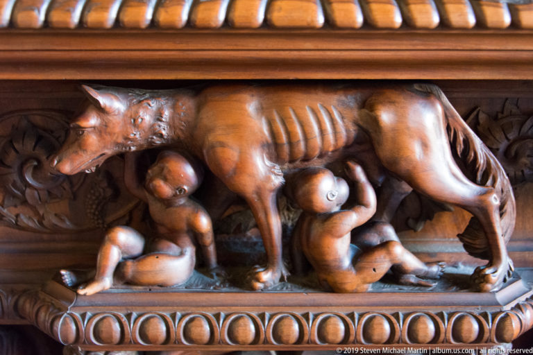 Carved wooden she-wolf standing over the nursing twins Romulus and Remus within a polished decorative panel.