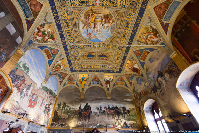 Decorated vaulted hall with military murals, mounted soldiers, painted arches, inscriptions, portraits, and elaborate ceiling panels.