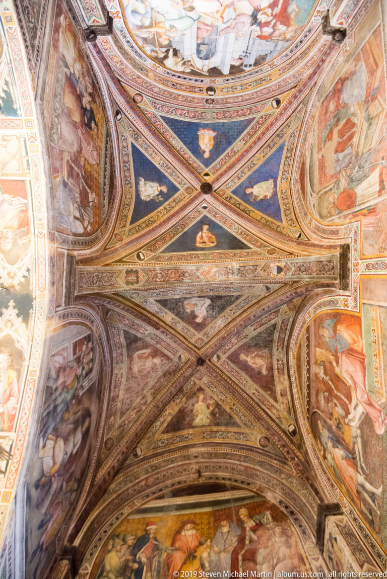 Cross-vaulted ceiling with richly painted ribs, blue fields, narrative frescoes, saints, and ornamental borders.