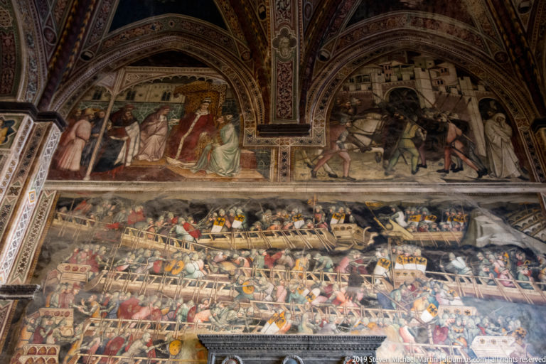 Large crowded fresco with upper arched scenes and a dense lower panorama of people, animals, buildings, and conflict.