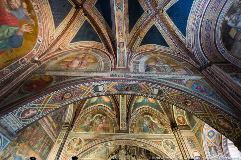 Upward view of intersecting painted arches and frescoed vaults filled with sacred figures, medallions, and geometric ornament.