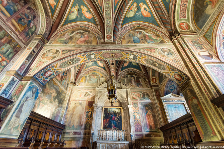 Fresco-covered chapel with a central marble altar, framed devotional painting, painted vaults, and dark wooden stalls along both sides.