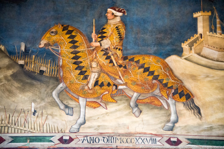 Guidoriccio da Fogliano rides a patterned horse across a fortified landscape in the celebrated Palazzo Pubblico equestrian fresco.
