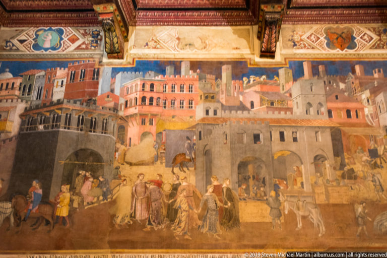 Ambrogio Lorenzetti fresco of a dense medieval city with towers, workshops, riders, workers, merchants, and pedestrians filling the streets.