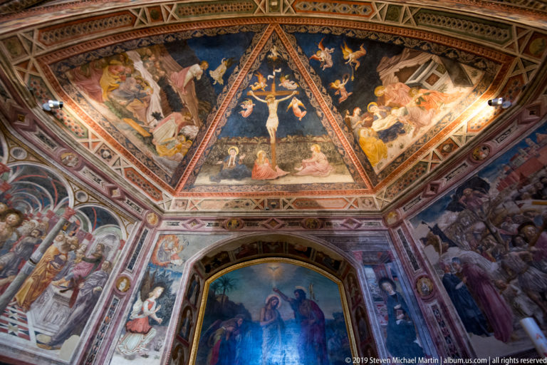 Upward view of a frescoed chapel with Crucifixion in the central vault field and narrative scenes covering surrounding walls.