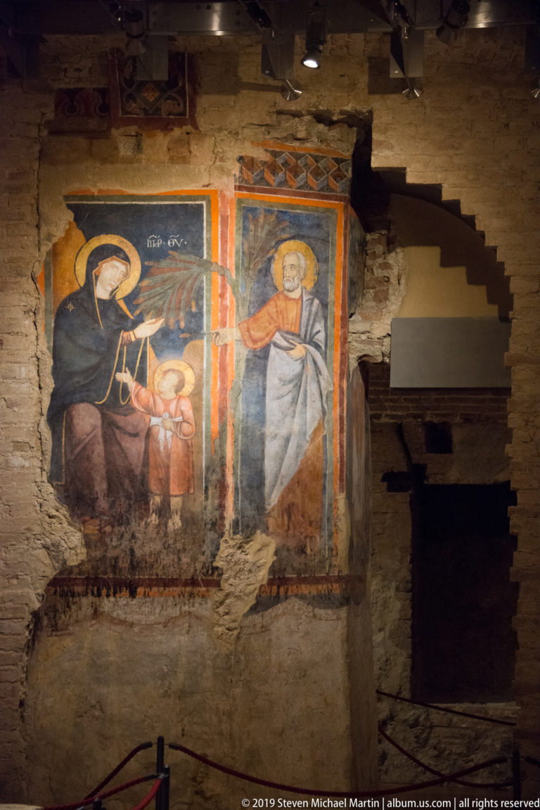 Two medieval fresco panels on rough masonry, with haloed figures in the larger left scene and a standing saint at right.