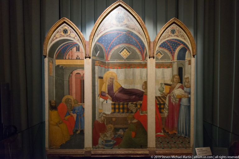 Pointed three-panel Gothic painting with a reclining central figure, attendants, side narratives, patterned blue fields, and red garments.