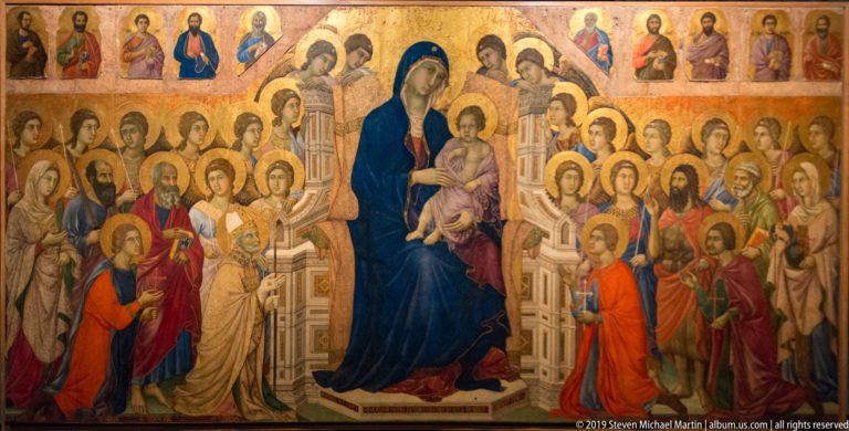 Gold-ground panel of enthroned Madonna and Child surrounded by dense ranks of haloed saints and angels.