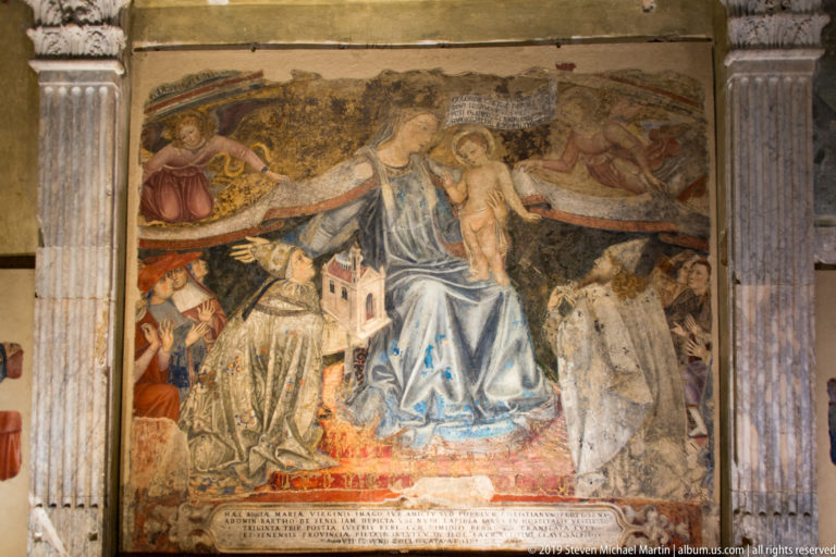 Fresco of the enthroned Virgin in blue with the Christ Child, surrounded by smaller figures, angels, and damaged painted architecture.