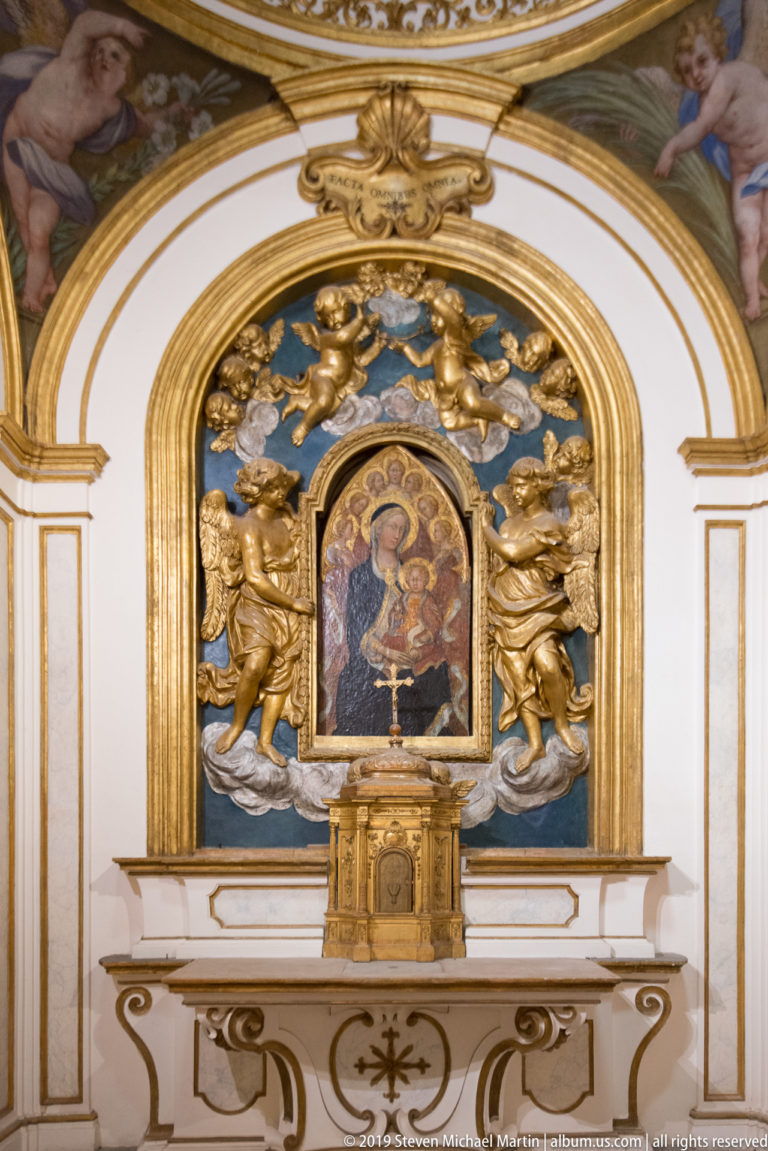 Gilded altar with a small central Madonna and Child image surrounded by sculpted angels, clouds, scrolls, and rays.