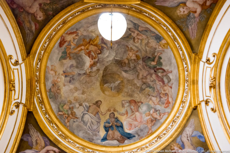 Frescoed circular dome filled with clouds, angels, and sacred figures, framed by gilded architectural moldings.