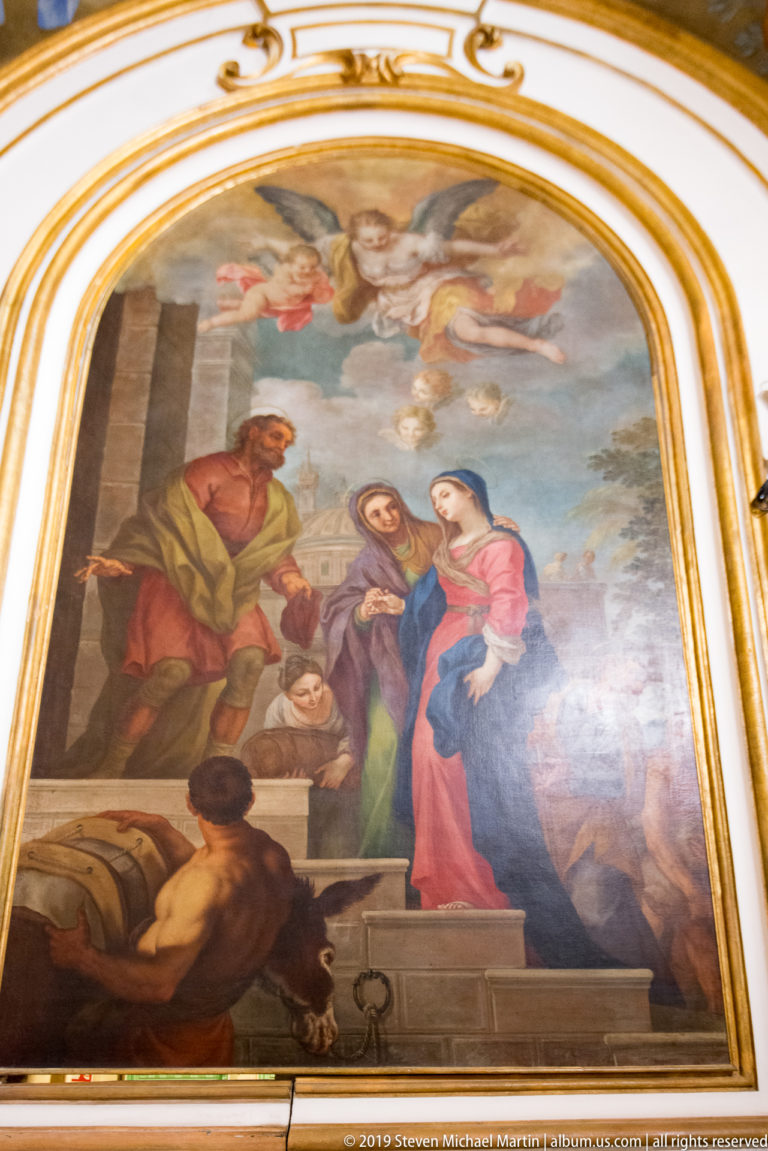 Arched religious painting with robed women gathered around a reclining figure and additional figures in clouds above.