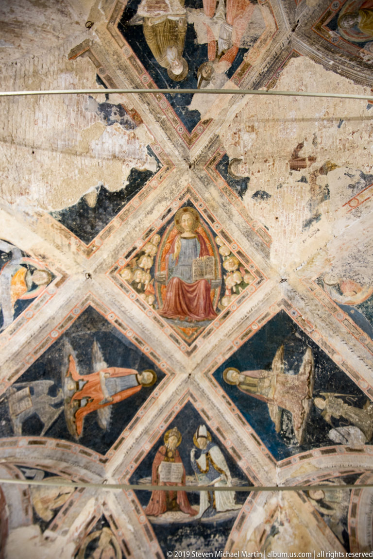 Medieval cross-vaulted ceiling with seated saints, symbolic creatures, patterned ribs, and worn fresco surfaces.