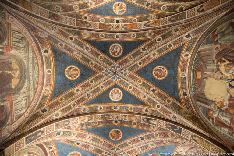 Blue painted vault crossed by ornate ribs and filled with circular figural medallions, rosettes, and patterned borders.