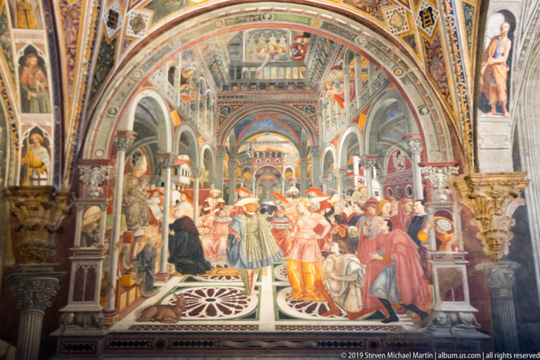 Fresco of clergy and officials assembled in a long arcaded hall with balconies, patterned pavement, and painted walls.