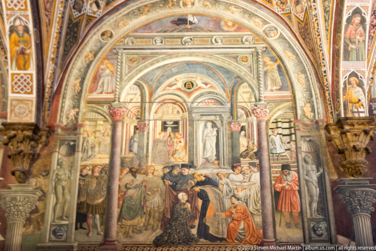 Fresco of caregivers, patients, visitors, and officials inside an ornate hospital hall of arches and painted niches.