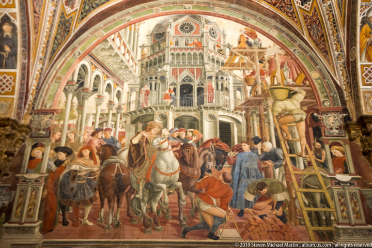 Fresco with riders on horseback and laborers working beside a ladder and building materials before an ornate civic structure.
