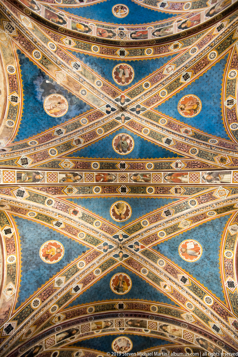 Close view of a blue cross-ribbed ceiling with circular portraits, small medallions, and densely patterned decorative bands.