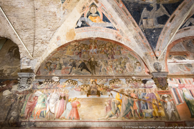 Large medieval wall fresco with crowded narrative scenes, rows of standing figures, and painted pointed vaults above.