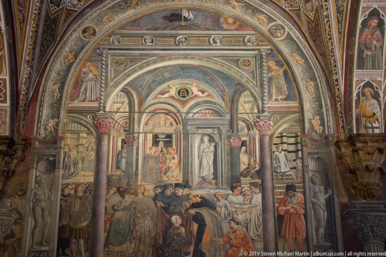 Fresco of attendants caring for reclining and seated people beneath layered arches and painted architectural niches.