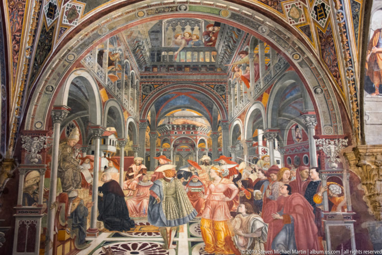 Fresco of clergy, officials, and attendants assembled in a richly decorated arcaded hall with patterned pavement and balconies.
