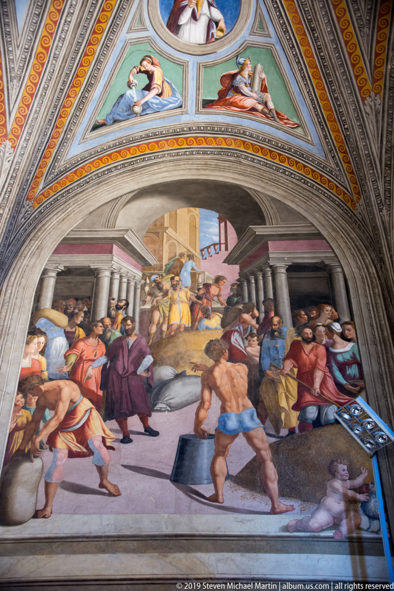 Fresco of workers and attendants carrying objects and moving through a large architectural interior with tables and open passages.