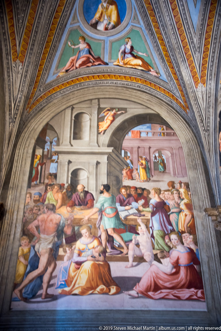 Fresco crowded with men and women beneath monumental arches, including a seated woman in the foreground and figures on stairs.