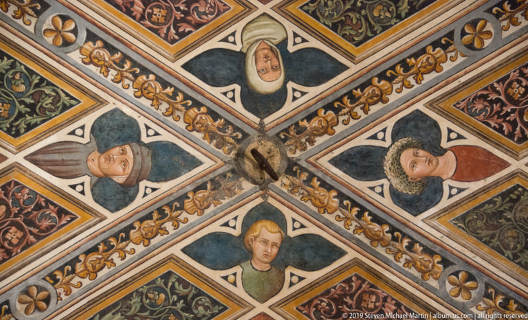Four painted human heads in diamond-shaped ceiling fields arranged around intersecting decorative ribs and floral panels.
