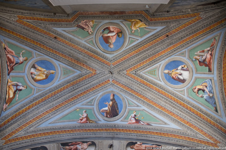 Painted groin vault divided by decorated ribs, with circular portraits and seated figures on blue and green grounds.