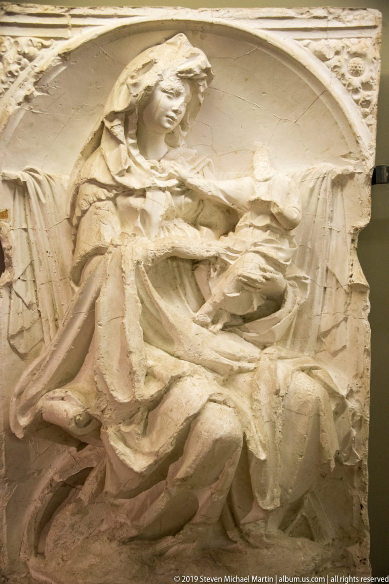 Fragmentary arched stone relief of the seated Virgin and Child with heavily eroded upper and central areas.
